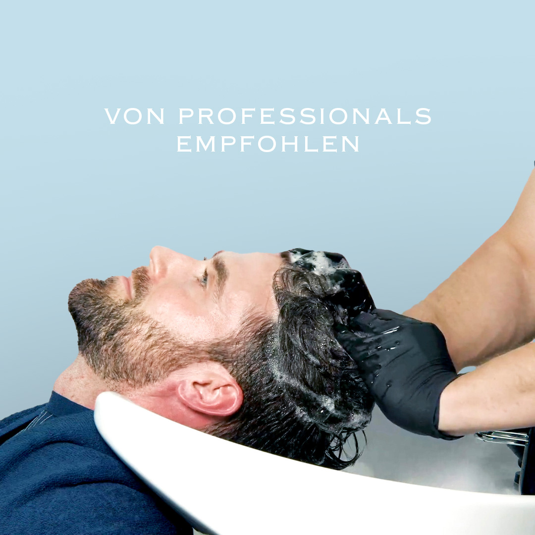 Mann bei professioneller Haarwäsche mit aufgeschäumtem Shampoo am Salonwaschbecken