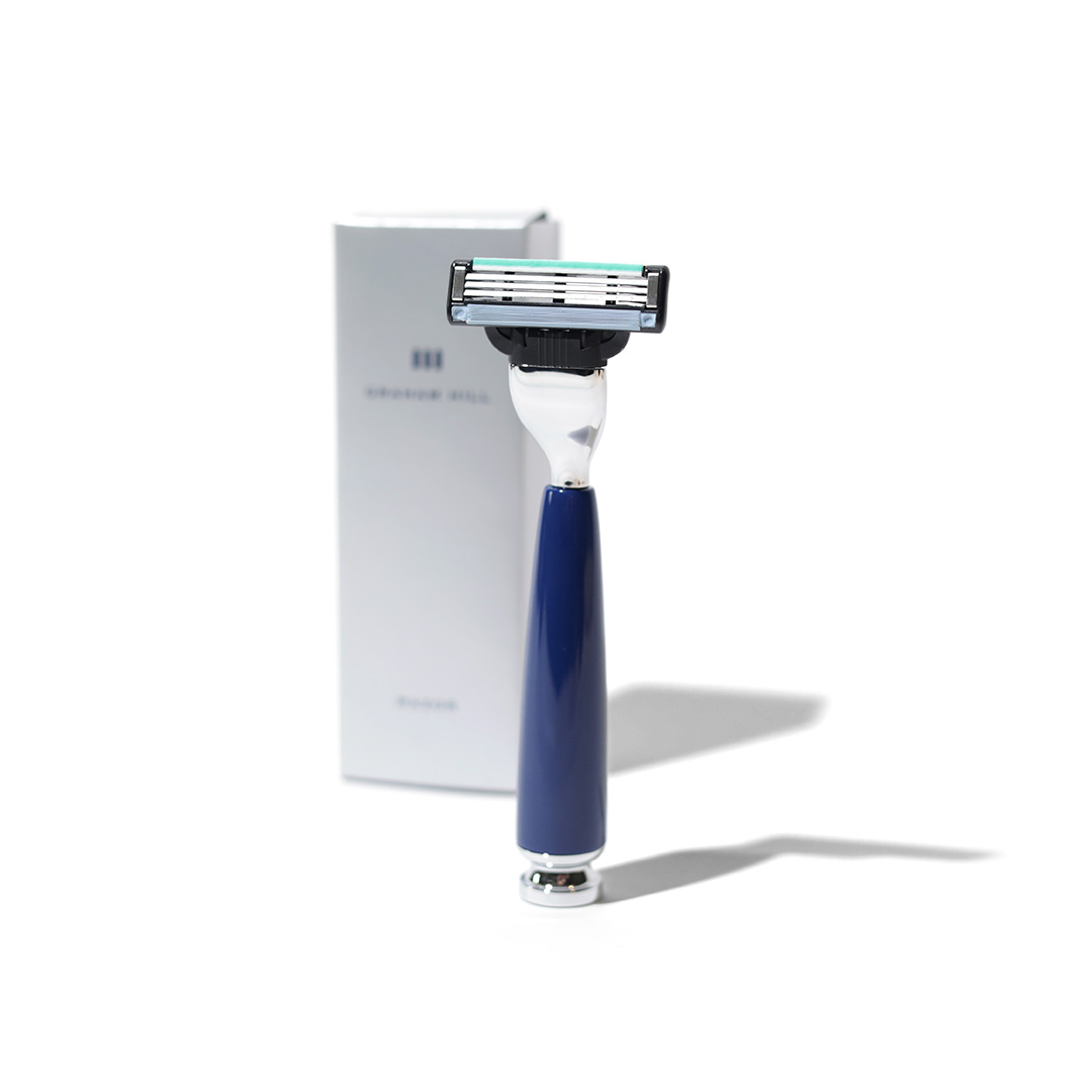 GRAHAM HILL RAZOR mit preussenblauem Edelharzgriff, silberfarbenen Details und Gillette Mach3 Klinge vor weisser Produktverpackung.