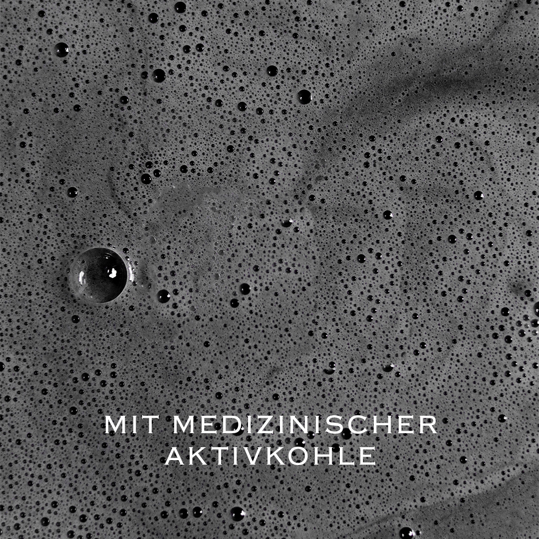 Dunkler Shampoo-Schaum mit feinen Blasen und dem Schriftzug „Mit medizinischer Aktivkohle“